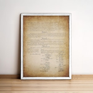 May include: A vintage-style print of the United States Constitution, featuring the text of Articles V, VI, and VII, along with the signatures of the Founding Fathers. The document is framed in a white frame and has a distressed, aged appearance.