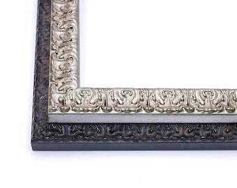 May include: Close-up of the corner of a double picture frame. The outer frame is black with a decorative pattern. The inner frame is silver with a more intricate pattern.