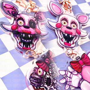 May include: Four acrylic keychains featuring cartoon characters with pink and white color schemes. The keychains depict a character with a wide grin and sharp teeth, and a robotic arm and bow. The background is a blue and white checkered pattern.