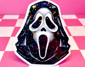 Pode incluir: Um autocolante holográfico com a máscara Scream. A máscara é branca com um capuz preto, decorado com glitter colorido em forma de estrela. O autocolante está numa superfície xadrez rosa e branca.