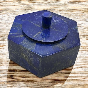 May include: A hexagonal lapis lazuli box with a lid and a knob on top. The box is made of polished lapis lazuli and has a deep blue colour.