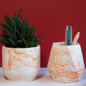 an orange concrete planter with flowers and an orange pen holder