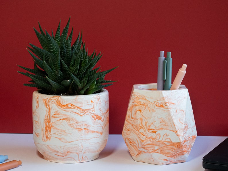 an orange concrete planter with flowers and an orange pen holder