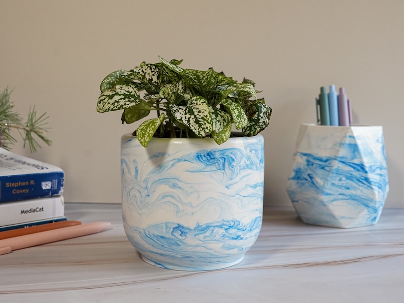 a blue concrete planter and a concrete pen holder with pens on a desk