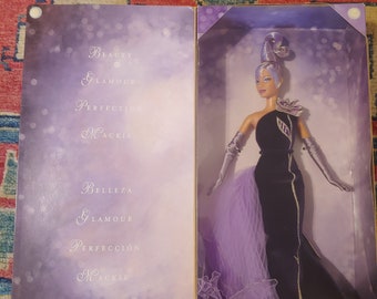 May include: A purple and black Barbie doll in a box. The box has the words "Beauty, Glamour, Perfection, Mackie" on it. The doll is wearing a black dress with a purple overlay and a silver tiara.