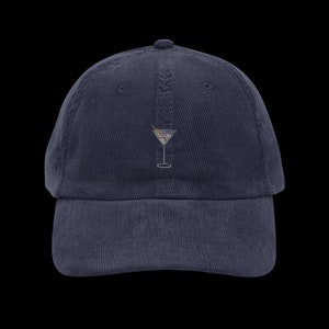 以下が含まれることがあります： 刺繍されたマティーニグラスのデザインが施されたネイビーブルーのコーデュロイベースボールキャップ