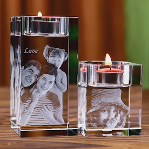 May include: Two clear glass candle holders with lit candles. One is rectangular and the other is square. Each has a family photo etched into the glass. The word "Love" is etched on the rectangular holder.