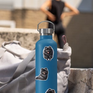 May include: A blue stainless steel water bottle with three black and white dog stickers. The stickers feature a Pomeranian dog in different poses.