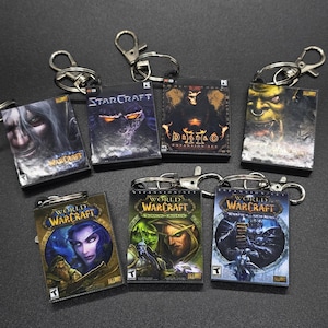 May include: Six keychains featuring video game covers. The keychains are silver with a black background and feature the following games: Warcraft, StarCraft, Diablo, World of Warcraft: Burning Crusade, World of Warcraft: Wrath of the Lich King, and World of Warcraft.