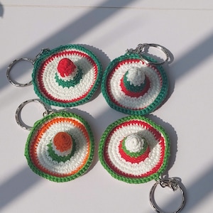 Op de afbeelding: Vier gebreide sombrero sleutelhangers met groene, witte en rode strepen. Elke sleutelhanger heeft een kleine gebreide sombrero bovenop.