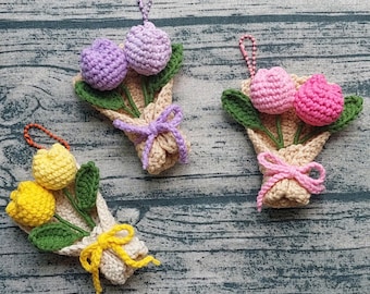 Può includere: Tre bouquet di tulipani all'uncinetto in giallo, rosa e viola. Ogni bouquet ha foglie verdi ed è avvolto in filo beige, legato con un fiocco abbinato. Ogni bouquet ha un piccolo anello di metallo per appenderlo.
