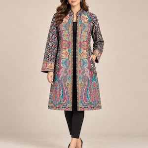May include: A long-sleeved, knee-length coat featuring a vibrant, multi-colored paisley and floral pattern in shades of teal, magenta, yellow, and black. The coat has a structured collar, a straight open front, and side pockets, worn over black pants.