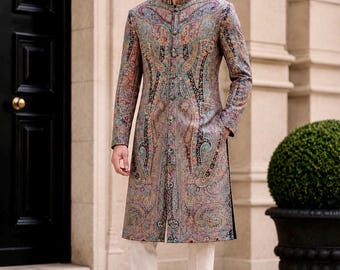 May include: A long-sleeved sherwani featuring a detailed, multi-colored paisley pattern in shades of blue, red, and gold. The garment has a high mandarin collar, a front button closure, and is paired with plain off-white trousers and brown shoes.