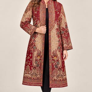 May include: A long-sleeved, knee-length open coat featuring a deep red and beige colour palette with intricate floral and paisley patterns throughout. The garment has a high collar, straight silhouette, and detailed border trim along the front edges.