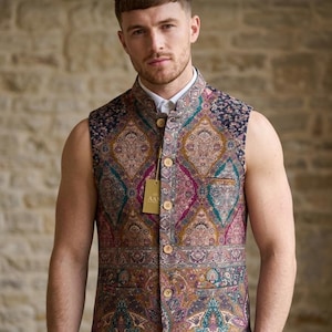 May include: A sleeveless vest featuring a vibrant paisley pattern in shades of magenta, teal, gold, and brown. The garment has a mandarin collar, a front button closure with light-colored buttons, and two front pockets. A small tag is attached.