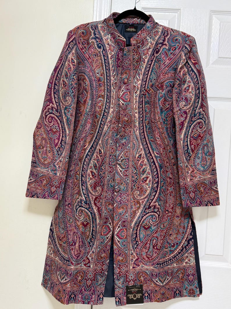 May include: A long-sleeved, knee-length coat featuring a mandarin collar and a front button closure. The garment is decorated with an intricate, multi-colored paisley pattern in shades of deep red, burgundy, navy blue, and teal on a textured fabric.