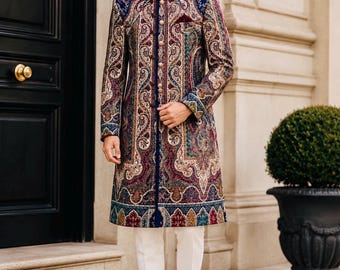 May include: A long-sleeved sherwani featuring a vibrant, multi-colored paisley pattern in shades of blue, red, gold, and cream. The garment has a high mandarin collar, a central row of metallic buttons, and is paired with plain white trousers.