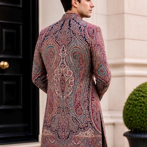 May include: A long-sleeved, high-neck jacket featuring a dark navy blue base with an intricate, multi-colored paisley pattern in shades of red, teal, and cream. The garment has a structured fit, a mandarin collar, and side slits at the hem.