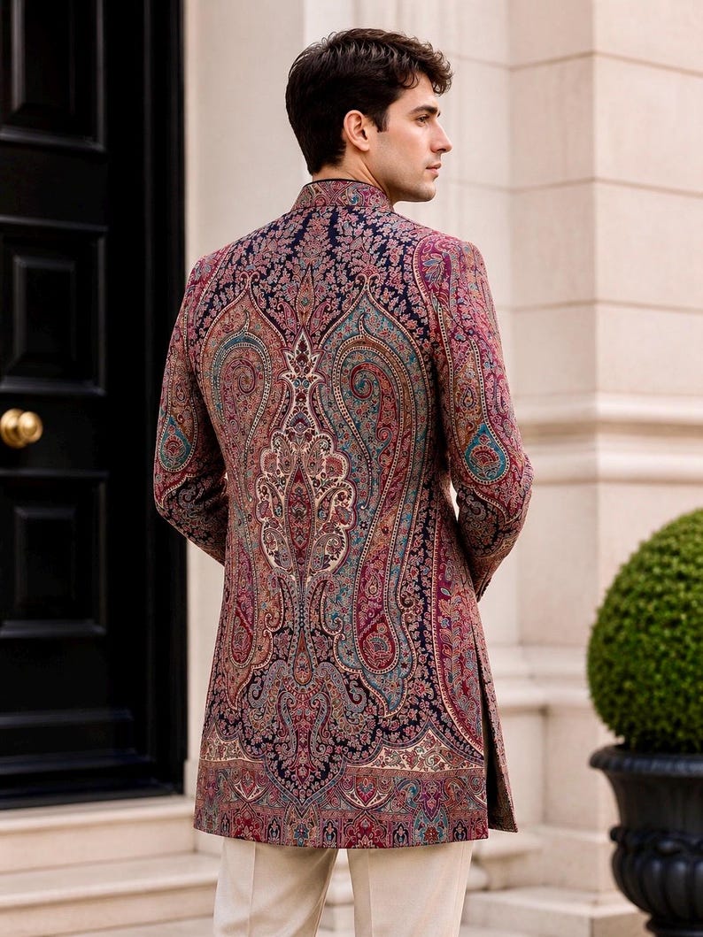 May include: A long-sleeved, high-neck jacket featuring a dark navy blue base with an intricate, multi-colored paisley pattern in shades of red, teal, and cream. The garment has a structured fit, a mandarin collar, and side slits at the hem.