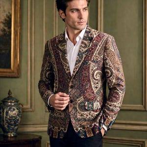 Könnte beinhalten: Gemusterter Blazer mit Paisley-Design in Beige, Burgunderrot und Blau. Der Blazer wird über einem weißen Hemd und einer schwarzen Hose getragen. Die Jacke hat einen Zwei-Knopf-Verschluss und ein fallendes Revers.
