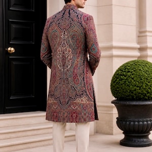 May include: A long-sleeved sherwani featuring a dark navy blue base with an intricate, multi-colored paisley pattern in shades of deep red, teal, and gold. The garment has a high mandarin collar and is paired with plain cream-colored trousers.