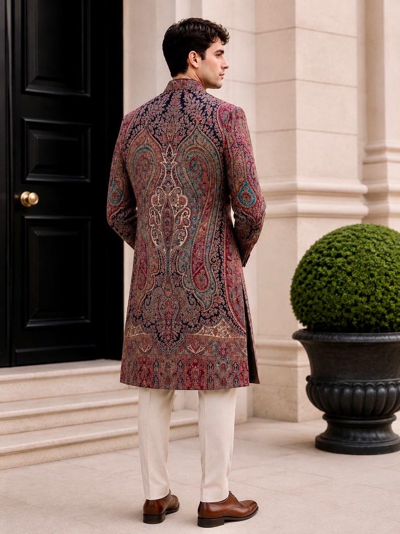 May include: A long-sleeved sherwani featuring a dark navy blue base with an intricate, multi-colored paisley pattern in shades of deep red, teal, and gold. The garment has a high mandarin collar and is paired with plain cream-colored trousers.