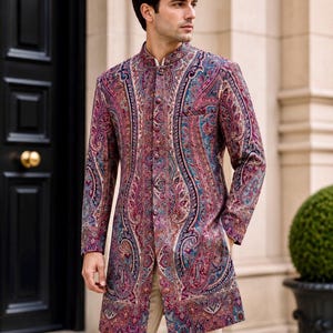 May include: A long-sleeved sherwani jacket featuring a vibrant, multi-colored paisley pattern in shades of deep magenta, teal, and purple. The garment has a high mandarin collar, a front button closure with matching fabric buttons, and light beige trousers.