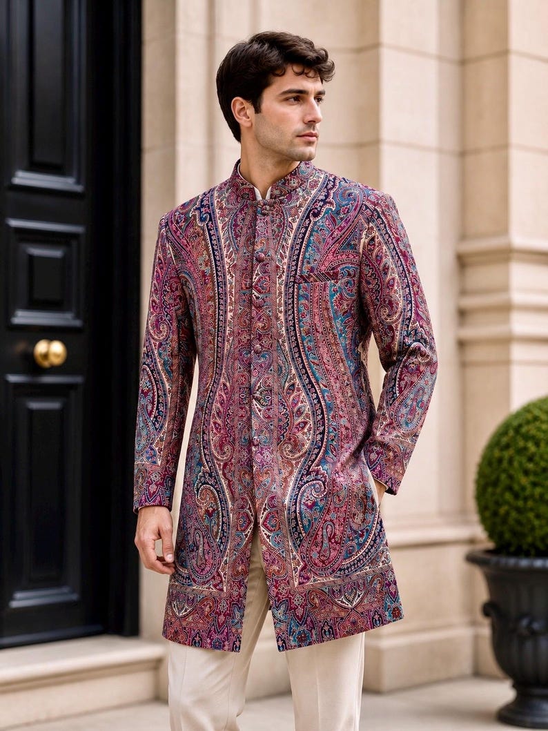 May include: A long-sleeved sherwani jacket featuring a vibrant, multi-colored paisley pattern in shades of deep magenta, teal, and purple. The garment has a high mandarin collar, a front button closure with matching fabric buttons, and light beige trousers.