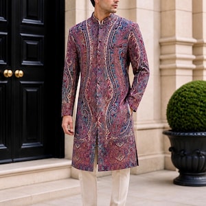 May include: A long-sleeved, knee-length sherwani jacket featuring a vibrant, multi-colored paisley pattern in shades of deep red, purple, and blue. The garment has a high mandarin collar, a front button placket, and is paired with slim-fit cream trousers.
