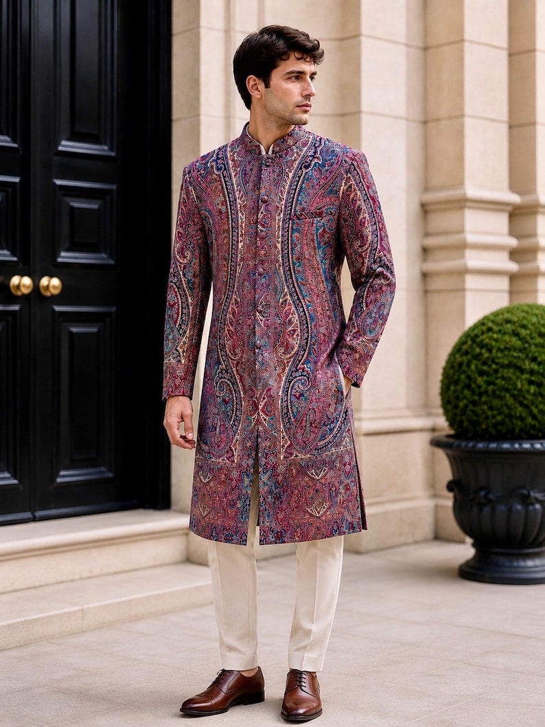 May include: A long-sleeved, knee-length sherwani jacket featuring a vibrant, multi-colored paisley pattern in shades of deep red, purple, and blue. The garment has a high mandarin collar, a front button placket, and is paired with slim-fit cream trousers.