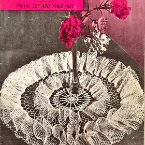 May include: A vintage crochet pattern book cover featuring a white crocheted doily with a pink flower arrangement in a glass vase. The cover text reads "Paragon Crochet Book 108, A Selection of New Attractive Doilies, together with Cheval Set and Table Mat, Full Working Instructions Inside, Price Code 'R'".