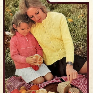 May include: Vintage book cover titled "A family affair in Caressa" featuring a woman and a child. The woman wears a yellow cardigan, and the child wears a pink sweater and white skirt. A picnic basket with food is in the foreground.