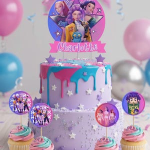 Può includere: Una torta di compleanno a due piani con gocce di glassa rosa e blu, sormontata da una decorazione a forma di stella con personaggi dei cartoni animati e il nome "Charlotte". Cupcake con glassa rosa e blu e decorazioni di personaggi.