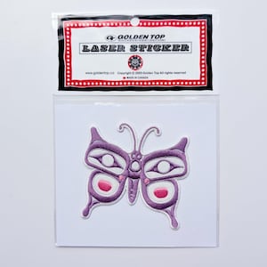 May include: A purple butterfly laser sticker with pink and white accents. The sticker is packaged in a clear plastic sleeve with a black and red border. The text "GOLDEN TOP" and "LASER STICKER" are visible.