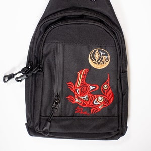 Peut inclure: Sac à bandoulière noir avec un motif brodé rouge et or d'un oiseau et d'une lune. Le sac a une poche zippée sur le devant et une fermeture zippée en haut.