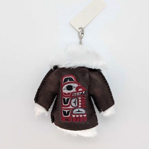 May include: A small brown coat with white faux fur trim and a Native American design on the back. The coat is attached to a silver keyring and a blank tag.