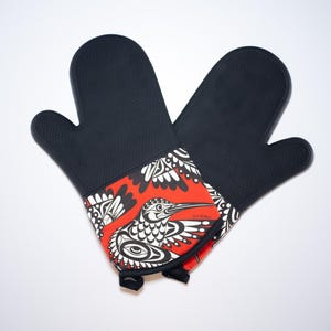 May include: A pair of black silicone oven mitts with a red and white patterned design featuring a bird. The pattern is a stylised design of a bird with wings spread.
