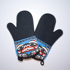 May include: A pair of black oven mitts with a blue and red design featuring a stylized animal face. The mitts are made of silicone and have a textured surface.