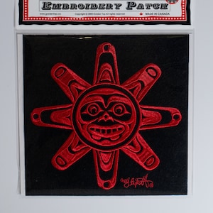 Peut inclure: Patch brodé rouge représentant un soleil stylisé avec un visage, sur fond noir. Le patch est étiqueté "Golden Top Embroidery Patch" et "Fabriqué au Canada".