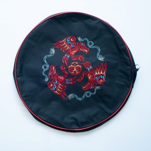May include: A black circular drum bag with a red trim. The bag features an embroidered design of three stylised birds with a central sun face. The birds are red, blue and yellow.