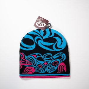 May include: A black knit beanie with a blue and pink design featuring a stylized animal. The beanie has a tag attached with the text "Proudly made in Canada with Canadian Wool."