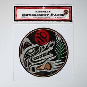 以下が含まれることがあります： 白い狼のデザイン、赤い太陽、緑の葉が刺繍された丸い黒いパッチ。パッチには「Golden Top Embroidery Patch」と「Made in Canada」のラベルが貼られています。