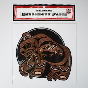 Può includere: Toppa ricamata con un orso marrone che tiene un salmone in bocca, circondata da un cerchio nero con un contorno argentato. La toppa è etichettata "Golden Top Embroidery Patch" e "Made in Canada".