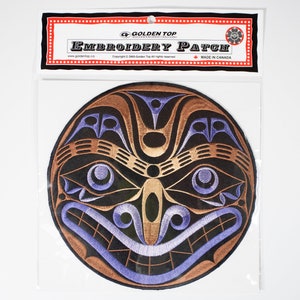 以下が含まれることがあります： 濃い青と金のスタイリッシュな顔のデザインが施された丸い刺繍パッチ。パッチには「Golden Top Embroidery Patch」と「Made in Canada」のラベルが付いています。