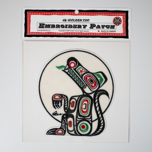 May include: A round, white embroidered patch featuring a black and green stylised wolf design. The wolf is howling and has red accents. The patch is labelled "Golden Top Embroidery Patch" and "Made in Canada".