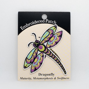 Puede incluir: Parche bordado con una libélula morada, azul y amarilla con el texto "Dragonfly" y "Maturity, Metamorphosis & Swiftness" debajo de la imagen.