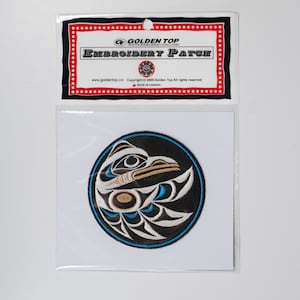 May include: A round, black and white embroidered patch with a blue outline. The patch features a stylized design of a bird's head with a beak and feathers. The text "Golden Top Embroidery Patch" is printed on the packaging.