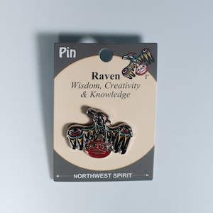 May include: A silver pin with a colorful raven design. The pin features a black raven with yellow, red, and blue accents. The text on the card reads "Raven, Wisdom, Creativity & Knowledge" and "Northwest Spirit".