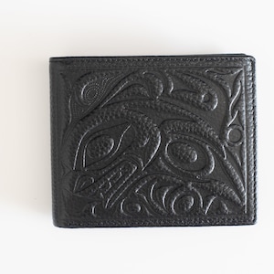 Könnte beinhalten: Schwarze Ledergeldbörse mit einem geprägten Design im indianischen Stil. Die Geldbörse hat ein detailliertes Muster aus stilisierten Vögeln und anderen Formen. Die Geldbörse ist rechteckig und scheint neu zu sein.