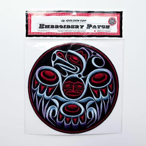 May include: Embroidered patch with a circular Native American design. The patch has a black background with red, blue, and white details. The text "EMBROIDERY PATCH" is visible at the top. Made in Canada.
